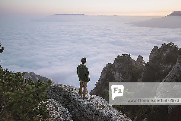 Junger Mann steht auf einem Berg über dem Nebel