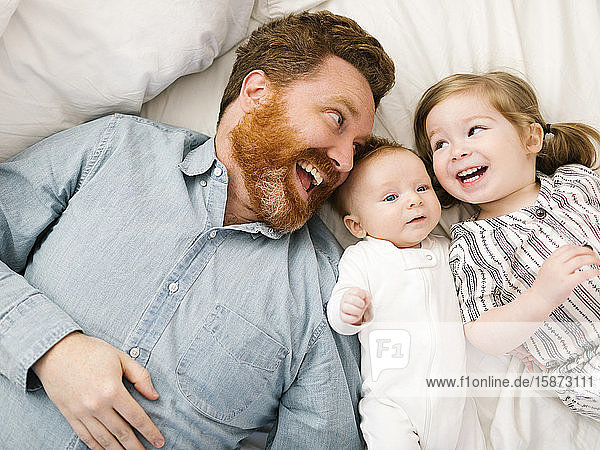 Vater und Kinder (2-3 Monate  2-3) liegen auf dem Bett und lachen