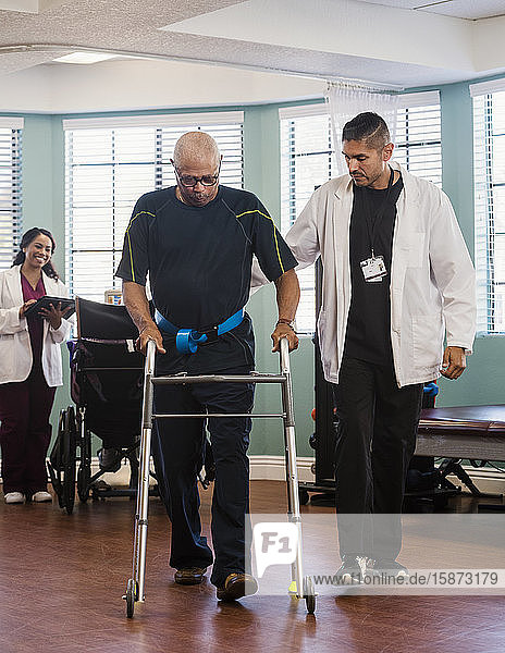 Arzt hilft älterem Mann bei der Benutzung einer Gehhilfe