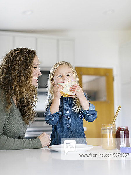 Lächelnde Frau beobachtet Tochter beim Essen eines Sandwichs