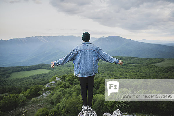 Mann steht auf einer Klippe neben Berg und Wald