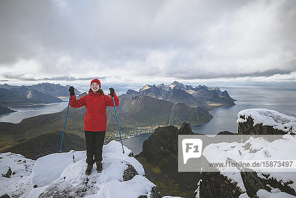 Junge Frau in roter Jacke mit Wanderstöcken auf verschneitem Berg