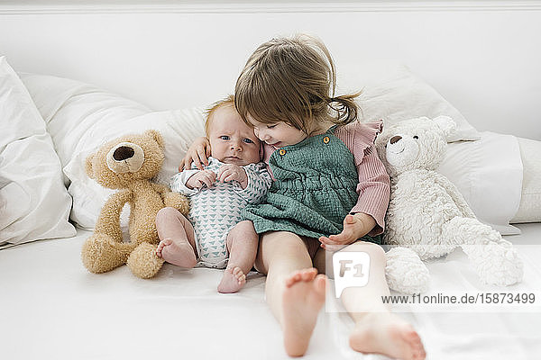 Siblings (2-5 months 2-3) sitting on bed with teddy bears