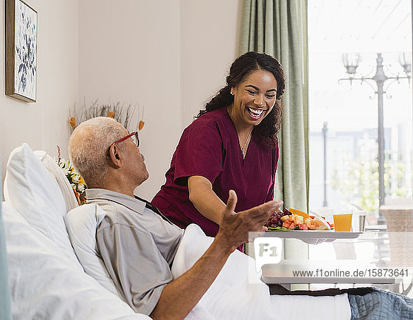 Smiling nurse hanging food to senior man in bed
