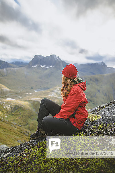 Junge Frau in roter Jacke auf einem Berg sitzend