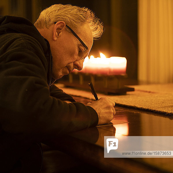Senior man writing letter by candlelight