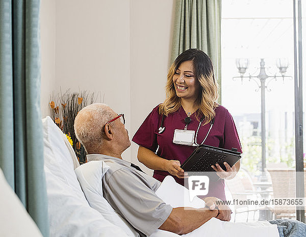 Lächelnde Krankenschwester hält Klemmbrett neben einem älteren Mann im Bett