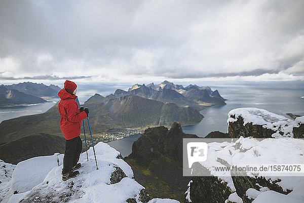 Junge Frau in roter Jacke mit Wanderstöcken auf verschneitem Berg