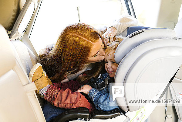 Woman kissing son in car seat