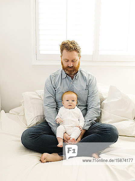 Father sitting on bed with baby boy (2-3 months)