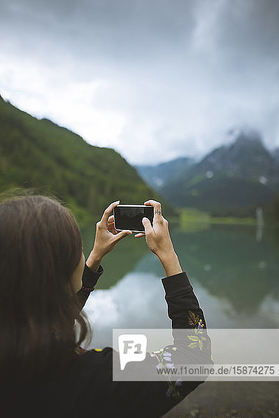 Junge Frau fotografiert Berg und See mit Smartphone