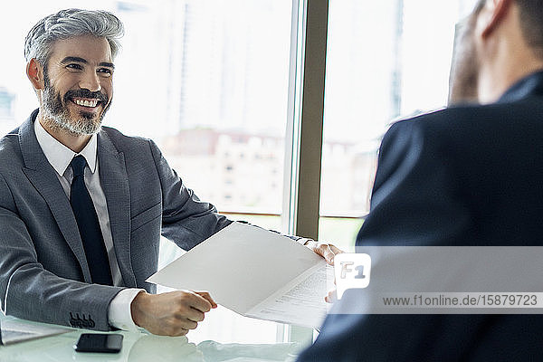 Ein lächelnder Geschäftsmann zeigt seinem Kollegen ein Dokument