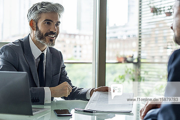 Smiling businessman showing document to his colleague