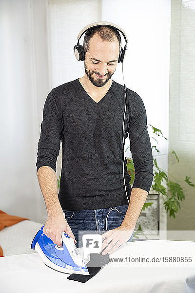 Ein Mann bügelt  während er Musik hört und lächelt.