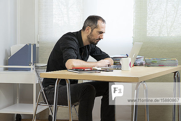 Mann  der in gebückter Haltung an seinem Schreibtisch sitzt.