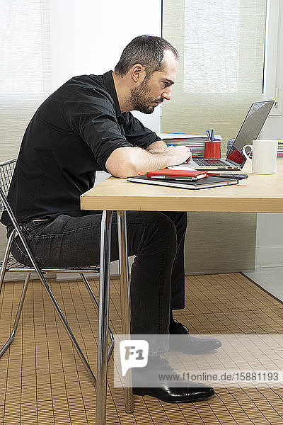 Mann  der in gebückter Haltung an seinem Schreibtisch sitzt.