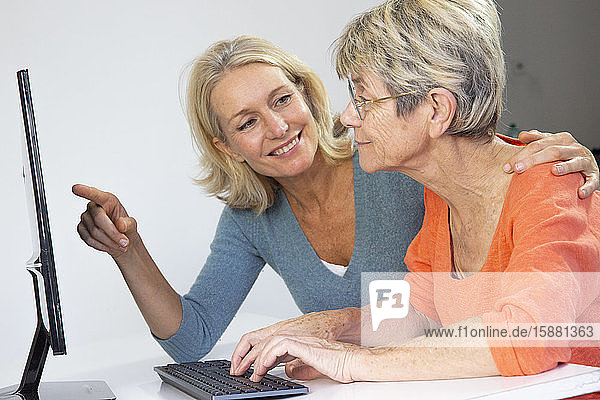 Eine Frau in den Fünfzigern hilft einer älteren Frau bei der Benutzung eines Computers.
