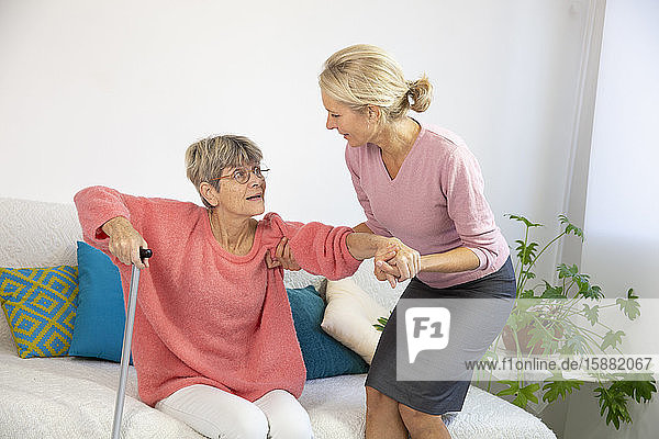 Eine Frau in den Fünfzigern hilft einer älteren Frau beim Aufstehen.