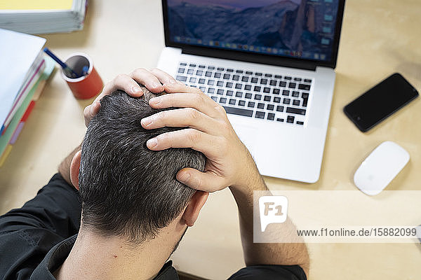 Ein Mann  der seinen Kopf in den Händen hält  sitzt vor seinem Computer.