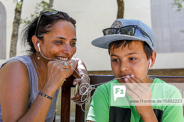 Mutter und Sohn führen ein Handygespräch und teilen sich Kopfhörer in Sizilien (Italien).