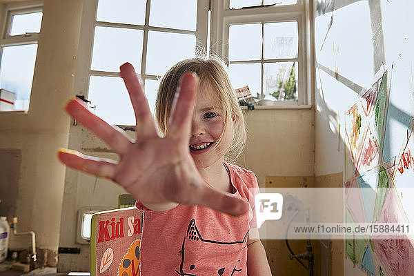 Lächelndes Mädchen im Haus während der Corona-Virus-Krise  Fingerfarben malen  in die Kamera schauen.