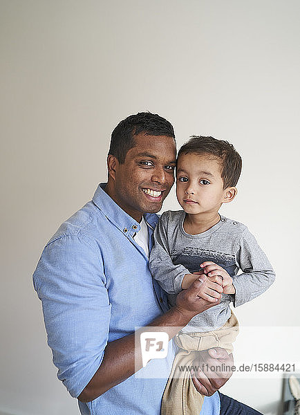 Ein Mann hält seinen Sohn und lächelt  während beide in die Kamera schauen.