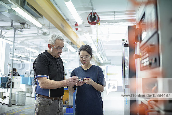 Männliche und weibliche Ingenieure stehen in der Fabrik neben der CNC-Drehmaschine.