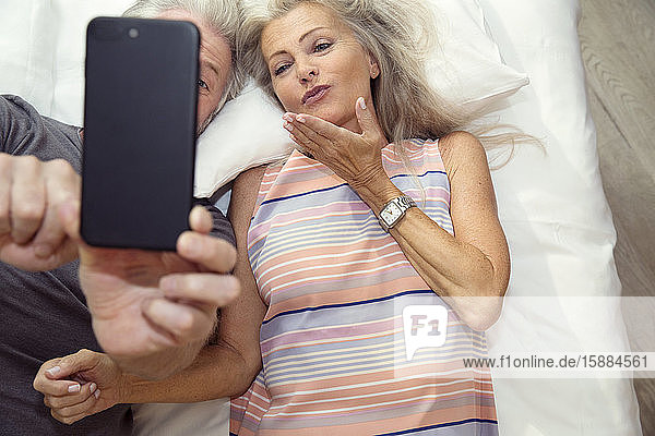 A couple lying on a bed taking a selfie on a mobile phone.