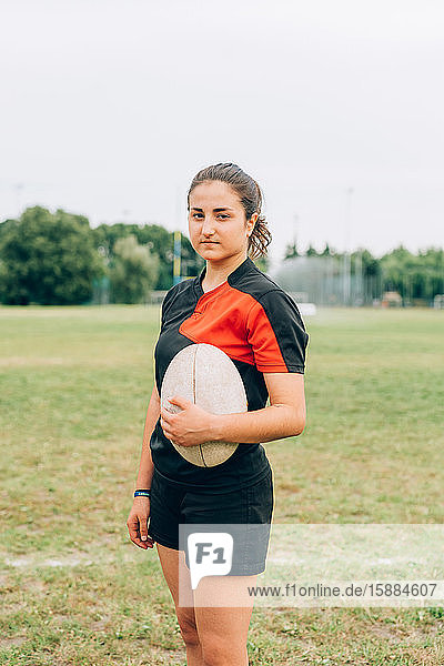 Eine Frau  die in Shorts und T-Shirt auf einem Trainingsplatz steht und einen Rugbyball hält.