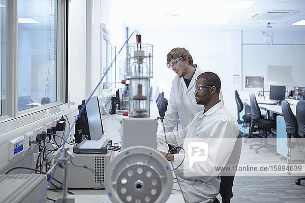 Zwei Männer in Laborkitteln an einem Schreibtisch mit Blick auf einen Computerbildschirm.