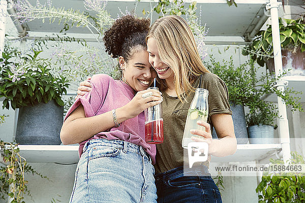 Zwei Frauen  die eng beieinander stehen und auf einer Terrasse ein Getränk trinken