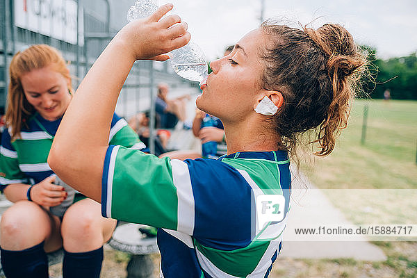 Eine Frau trägt ein blau-weiß-grünes Rugbyhemd und trinkt aus einer Wasserflasche