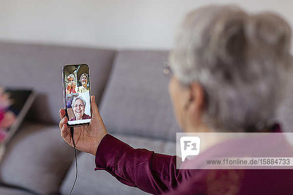 Eine Frau  die ein Mobiltelefon hochhält und drei Freunde auf dem Bildschirm betrachtet  während sie in sozialer Isolation  beim Skypen oder bei einer Dingsbums-Party ist.