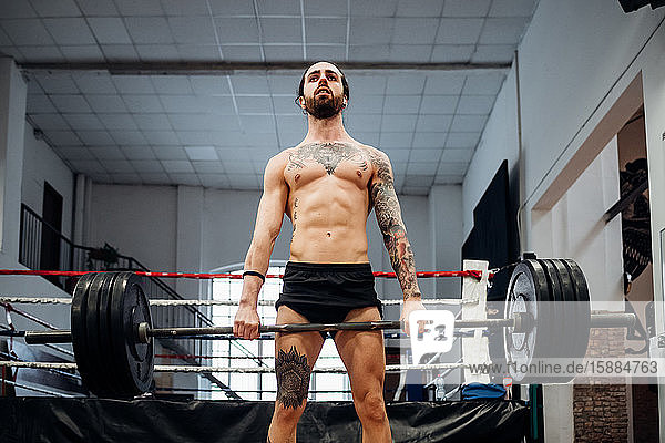 A man wearing black shorts with tattooed chest  arm and thigh holding a bar with heavy weights.