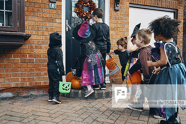 Eine Gruppe von Kindern  die sich zu Halloween an einer Haustür mit Eimern Trick oder Treating verkleidet haben.