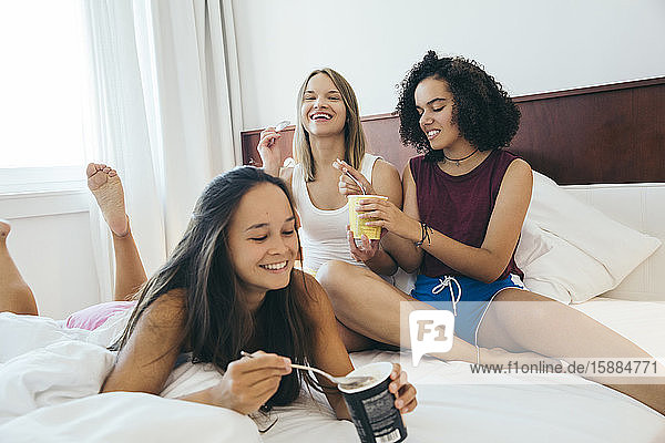 Frauen auf einem Bett  die lächeln und aus Eiscremekartons essen.