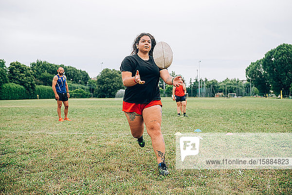 Rugby-Training  Frau fängt einen Rugby-Ball  während andere hinter ihr warten und der Trainer zur Seite steht.