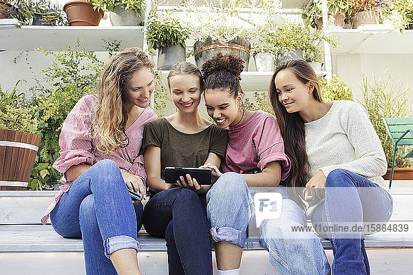 Four women sitting in a courtyard  looking at a phone and smiling.