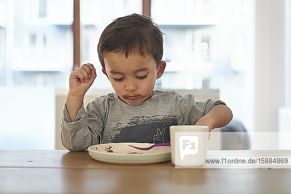A boy sitting at a table feeding himself with a fork from a plate.