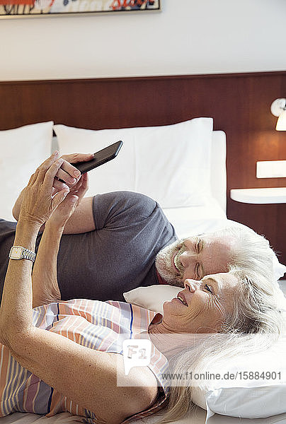 A couple lying on a bed looking at a mobile phone.