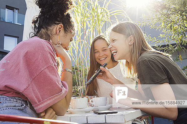 Drei Frauen sitzen um einen Tisch herum  schauen auf ein Mobiltelefon und lächeln.