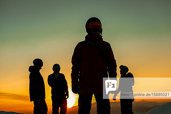 Vier Personen mit Skianzügen  Brillen und Helmen  die sich vor einem Sonnenuntergang abheben.