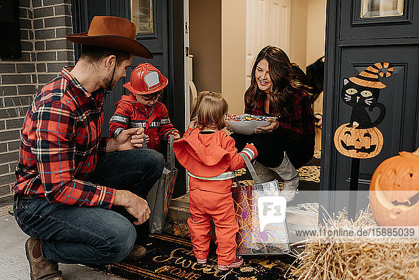 A family dressed up for Halloween trick or treating collecting sweets from a woman at her door.
