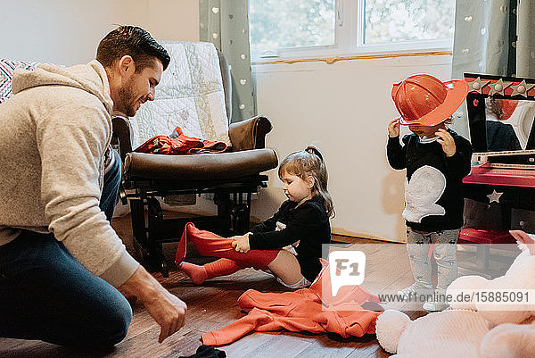 A father helping his two children getting dressed up as firefighters.