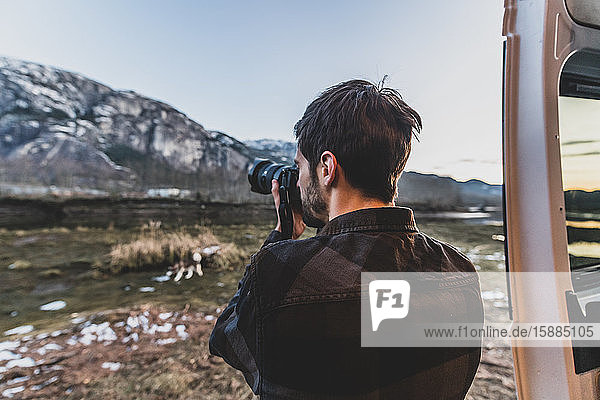 Man standing beside his van taking a picture of a rocky landscape.