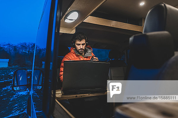 A man sitting in his campervan looking at an open laptop.