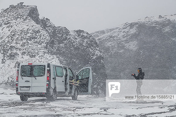 A person standing in a snowy wintry landscape taking a photograph of a campervan. Winter Surfing