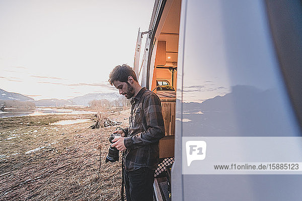 Ein Mann  der neben einem Lieferwagen steht und auf eine Kamera in seinen Händen blickt  im Hintergrund eine Felslandschaft.