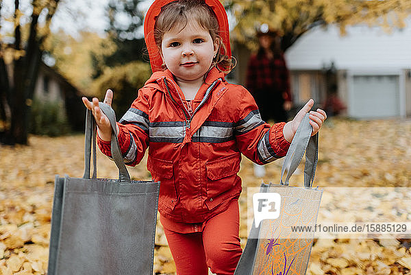 A child dressed as a firefighter for Halloween walks through a park with leaves on the ground.