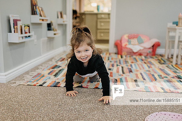 A young girl crawling towards the camera and smiling.